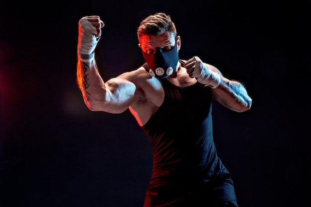 Fuerte atleta masculino en una máscara de entrenamiento negro sobre una pared negra