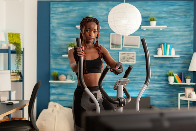 Fuerte atlético ajuste mujer negra haciendo ejercicio de entrenamiento cruzado en la sala de estar de casa usando eli moderno ...