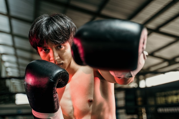 Fuerte joven parado con guantes de boxeo con puños en la arena