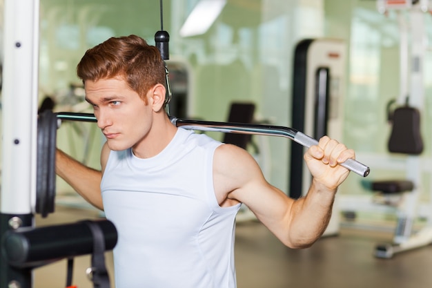 Fuerte y motivado. Hombre musculoso joven guapo trabajando en press de banca