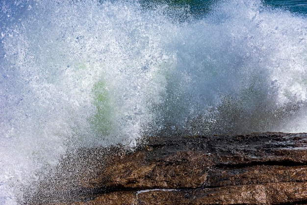 Fuerte ola chocando contra las rocas con agua de mar y espuma salpicando en el aire