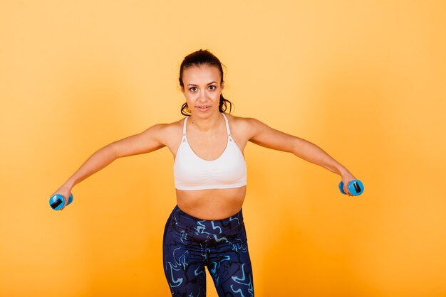 Fuerza y motivación. Longitud total de mujer africana joven y delgada en ropa deportiva haciendo ejercicio en estudio sobre fondo amarillo