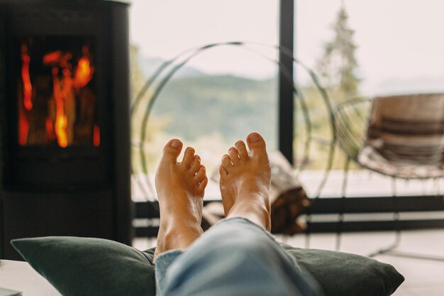 Füße am modernen Kamin und Fenster mit Blick auf die Berge Frau barfuß in gemütlichem Zuhause entspannen