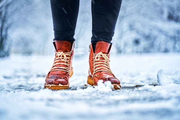 Füße einer Frau auf einem schneebedeckten Bürgersteig in braunen Stiefeln