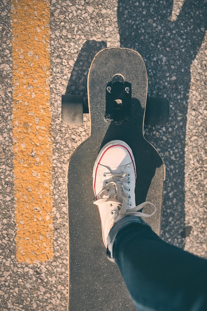 Füße einer Frau in Turnschuhen auf einem Longboard am Abend