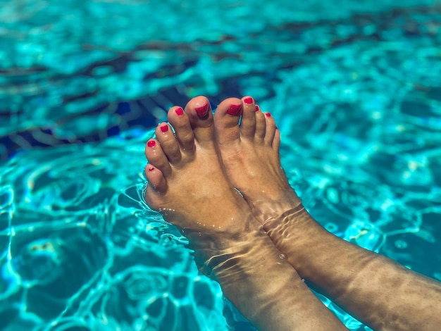 Füße eines Mädchens mit heller Pediküre im Pool, das in einem heißen tropischen Land im Wasser schwimmt