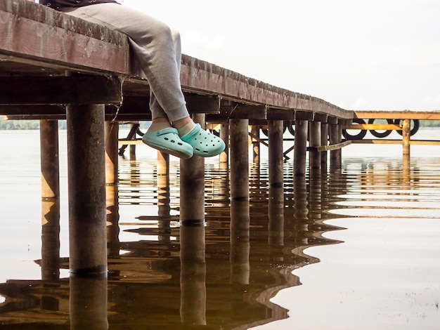 Füße eines Mannes, der auf einer Brücke am Fluss sitzt Das Konzept der Erholung