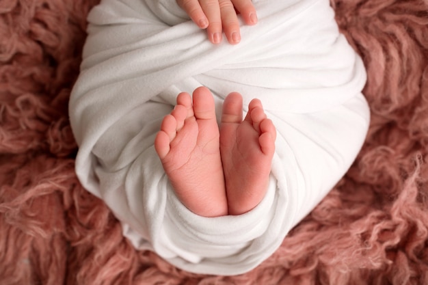 Füße eines neugeborenen Babys eingewickelt in eine weiße Decke. Behandeln Sie die Finger eines Neugeborenen. Foto in hoher Qualität