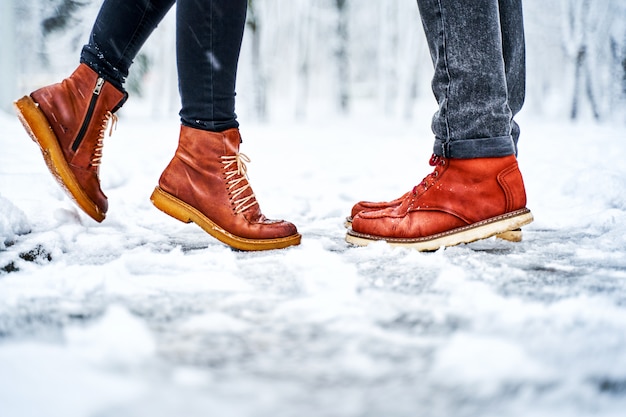 Füße eines Paares auf einem schneebedeckten Bürgersteig in den braunen Stiefeln