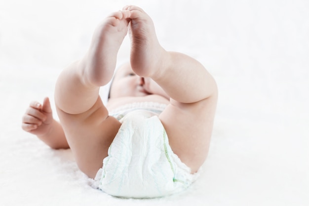 Füße eines sechs Monate alten Babys, das Windeln trägt, die auf dem Bett liegen