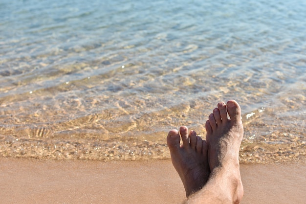 Füße im Sand am Strand gegen ein blaues Meer