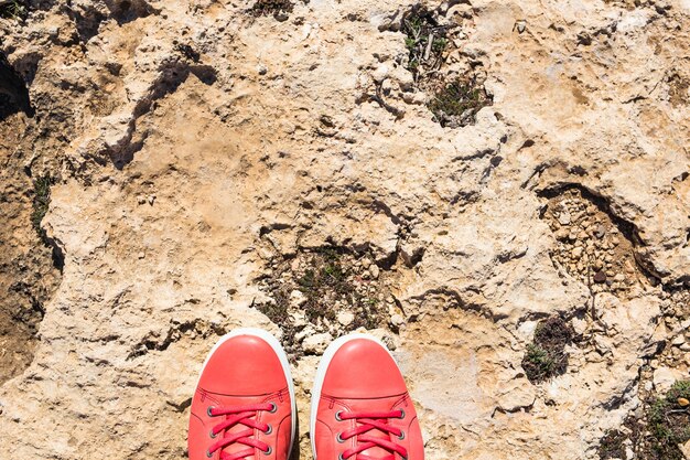 Füße in lässigen rosa Schuhen auf dem Steinhintergrund.