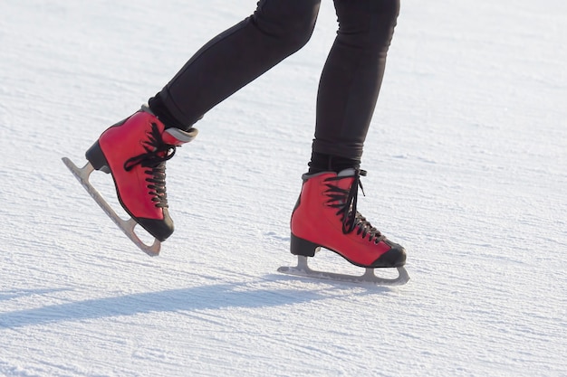 Füße in roten Schlittschuhen auf einer Eisbahn. Hobbys und Sport.