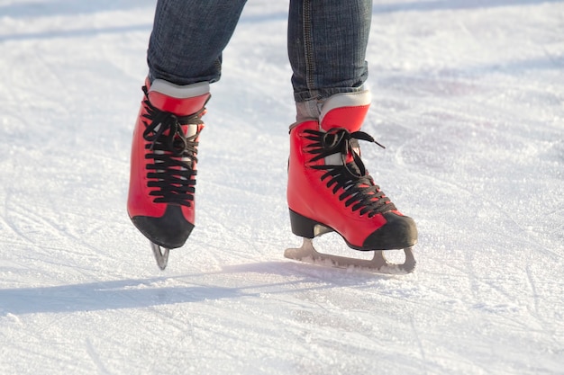 Füße in roten Schlittschuhen auf einer Eisbahn.