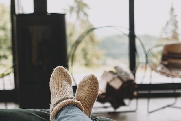 Füße in warmen, kuscheligen Socken auf dem Hintergrund eines modernen Kamins und Fensters mit Blick auf die Berge
