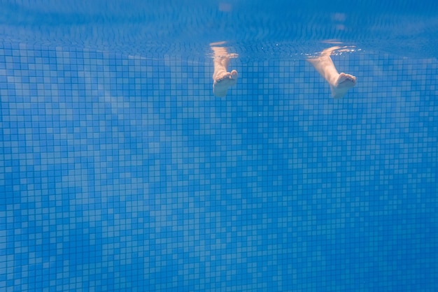 Füße von Menschen, die sich im Pool unter Wasser bewegen Kinderbeine Sommer Lustige Unterwasserbeine im Schwimmbad Unterwasseransicht von Frauen oder Kindern Urlaubs- und Sportkonzept