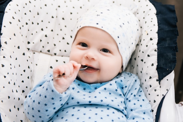 Füttern. Entzückendes Baby, das mit einem Löffel im Hochstuhl isst. Baby