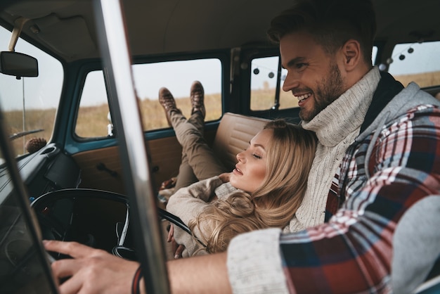 Fugindo de tudo ... mulher jovem e atraente descansando e sorrindo enquanto o namorado dirigia uma minivan estilo retro