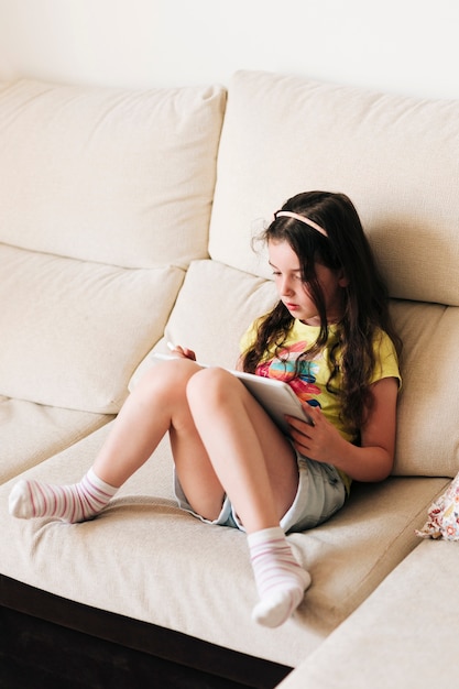 Foto full shot mädchen sitzt auf der couch mit ihrem tablet