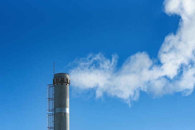 Fumaça branca da sala da caldeira de tubulação contra o fundo do conceito de mudança climática do céu azul