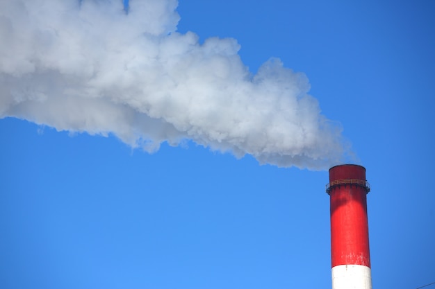 Fumaça branca vem de canos contra o céu azul