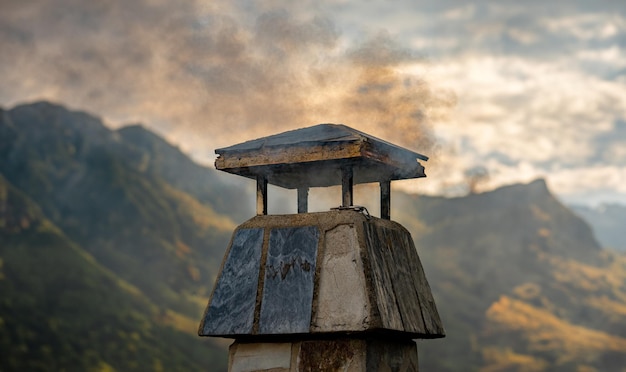 Fumaça de madeira preta saindo da chaminé de um telhado de uma casa rural no meio