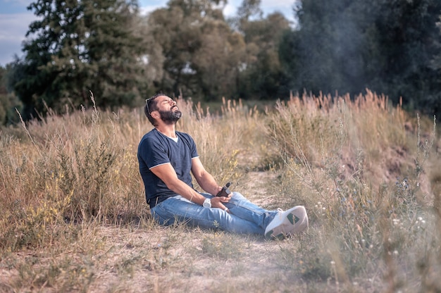 Fumador fumando un dispositivo de humo electrónico en el suelo del bosque