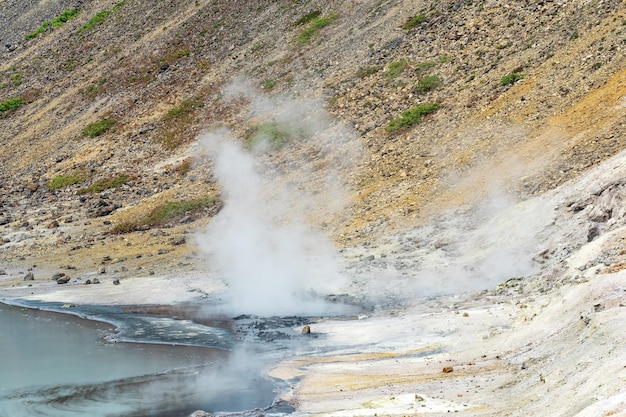 Fumarolas hirviendo y depósitos de azufre en la salida hidrotermal en la orilla del lago caliente en la caldera del volcán Golovnin en la isla de Kunashir