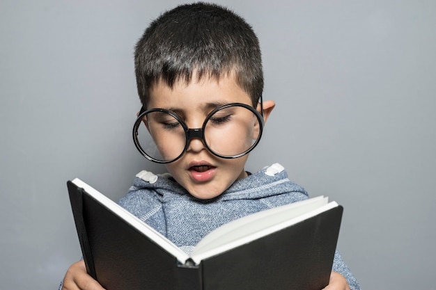 Fun Boy mit Riesenbrille beim Lesen eines Buches mit lustigen und abwechslungsreichen Gesten