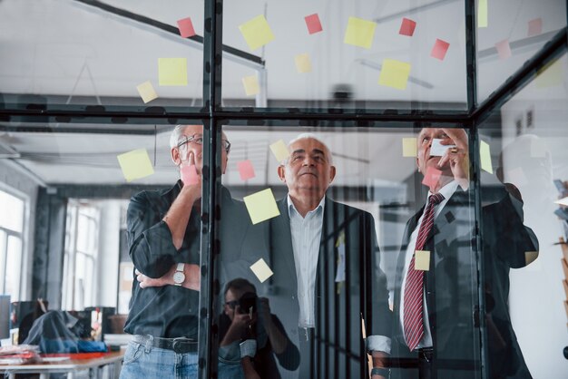 Funciona com adesivos no vidro. Equipe idosa de arquitetos empresários idosos tem uma reunião no escritório.