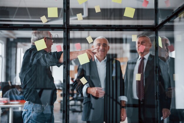 Funciona com adesivos no vidro. Equipe idosa de arquitetos empresários idosos tem uma reunião no escritório.