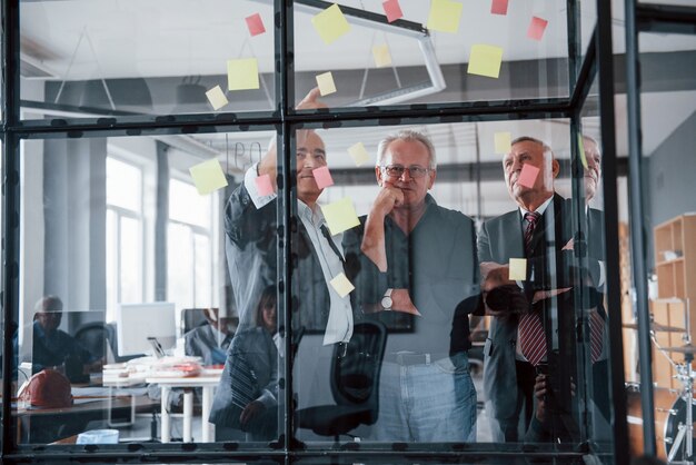 Funciona com adesivos no vidro. Equipe idosa de arquitetos empresários idosos tem uma reunião no escritório.