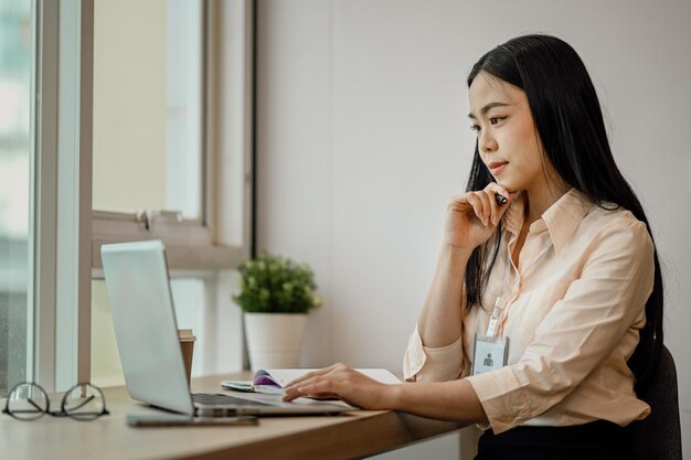 Funcionária asiática focada olhando para a tela do laptop lendo e-mail na mesa