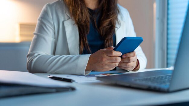 funcionária de escritório que usa blazer branco trabalhando até tarde no escritório enquanto manda uma mensagem para o telefone