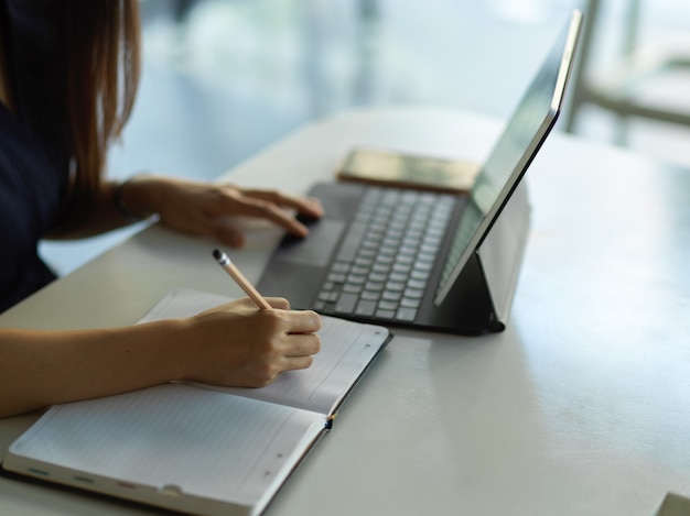 Funcionária de escritório torce a mão no notebook enquanto trabalha com o tablet digital