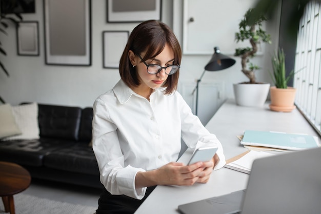 Funcionária europeia focada usando celular no local de trabalho no escritório mulher lendo e respondendo