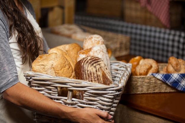 Foto funcionária segurando uma cesta de vime com vários pães no balcão de uma padaria