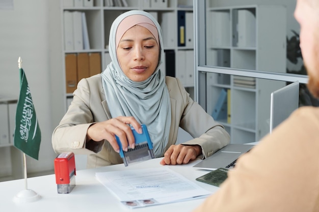 Funcionário consular muçulmano adulto jovem trabalhando na embaixada da arábia saudita dando aprovação para visto de viagem