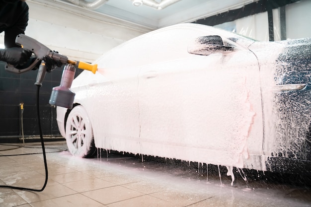 Funcionário da lavagem de carros aplica espuma no carro.