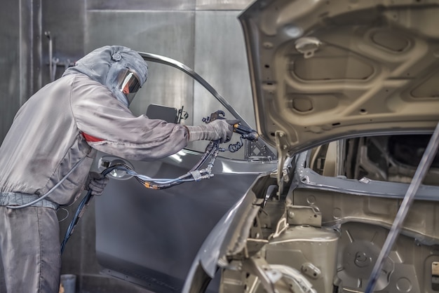 Funcionário da oficina de pintura da fábrica de automóveis pinta os elementos do carro.