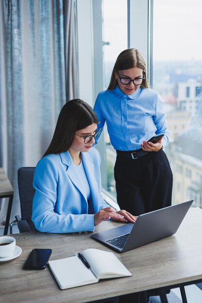 Funcionários alegres conversando enquanto trabalham em um laptop discutindo o trabalho durante uma pausa para o café no escritório uma mulher de negócios de óculos ouve um colega tem uma conversa agradável amizades