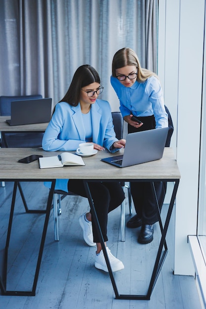 Funcionários alegres conversando enquanto trabalham em um laptop discutindo trabalho durante uma pausa para o café no escritório uma mulher de negócios de óculos ouve um colega tem uma conversa agradável amizades