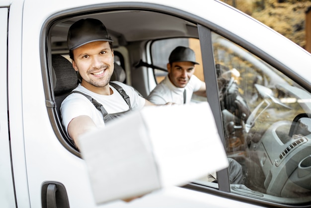 Funcionários da empresa de entrega alegre entregando mercadorias aos clientes em um veículo de carga, correio bonito olhando pela janela do carro com um pacote