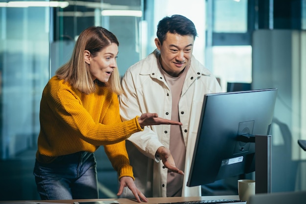 Funcionários da empresa de TI olham para o monitor do computador com surpresa, um homem asiático e uma mulher trabalham em um escritório moderno