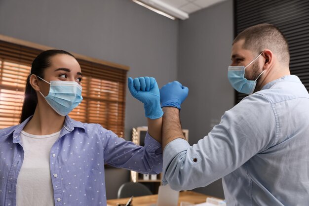 Foto funcionários de escritório com máscaras se cumprimentando batendo cotovelos no local de trabalho