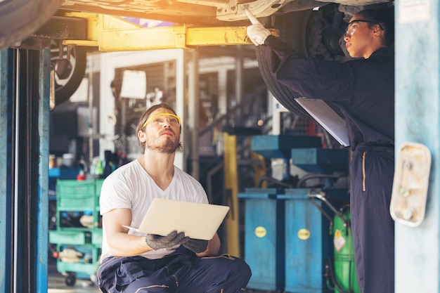 Funcionários do serviço de automóveis inspecionam a parte inferior e as placas de proteção sob o carro levantado