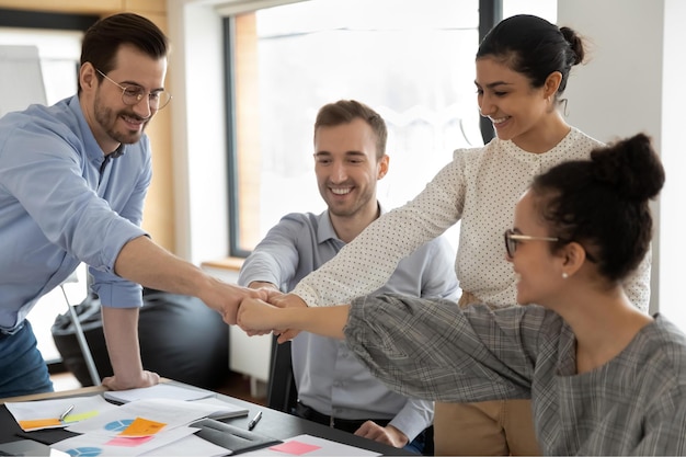 Foto funcionários muito felizes dão as mãos e dão punhos motivados para resultados de negócios em grupo compartilhados colegas multirraciais felizes envolvidos em atividade de formação de equipe em reunião no conceito de trabalho em equipe de escritório