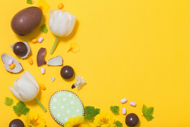 Fundo amarelo de páscoa com doces de ovos de chocolate e flores da primavera