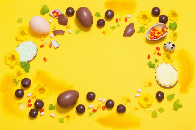 Fundo amarelo de Páscoa com ovos de chocolate, doces e spri