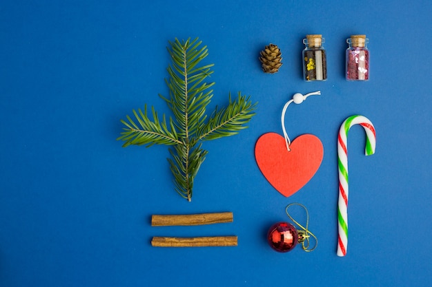 Fundo azul do Natal com galho de árvore do abeto, doces, garrafas de vidro com confete, coração, cones e canela. Estilo liso leigo. Cor do ano.